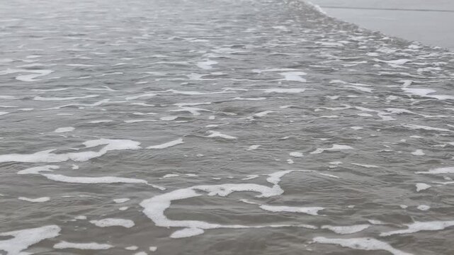 Close up of gentle ocean waves and white sea foam washing over a sandy beach. Peaceful coastal scene for travel and nature projects.