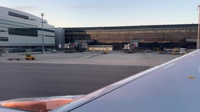 Airplane wing view on apron at Frankfurt Airport showing terminal gates, jet bridges and ground service vehicles in operation