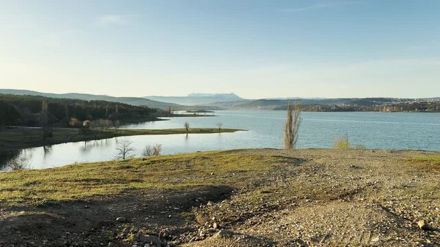 Calm blue waters stretch out toward hazy mountains under a clear sky. This expansive view feels peaceful and refreshing. The quiet landscape inspires a sense of freedom and serenity.