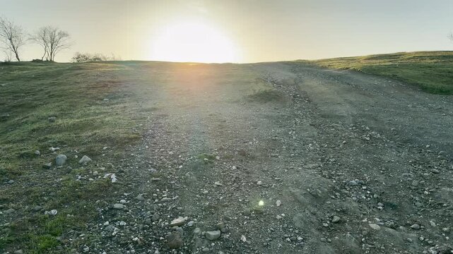 A bright sun shines over a rugged path on a quiet hill. This vast landscape feels hopeful and lonely. The warm glow creates a peaceful sense of a new beginning in the wild.