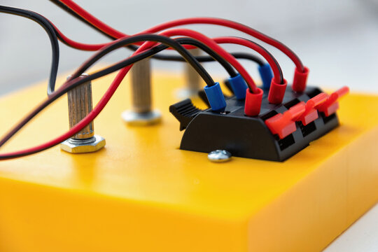 Close-up of red and black wires connected to a terminal block on a yellow base. Professional shot of electronics engineering and DIY connectivity