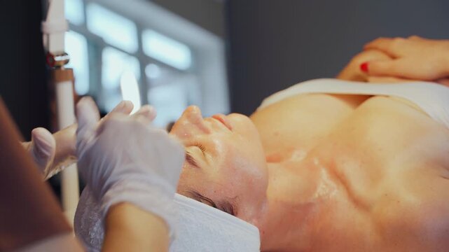 Clinic specialist applies peel and soothing mask on woman face with gloved hands, careful layering and timing, patient reclining under bright window light, post peel comfort preparation