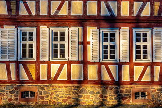 Fassade eines alten Fachwerkhauses im warmen Nachmittagslicht der Sonne mit Fenstern, Holzbalken, Gefachen und ge&ouml;ffneten Klappl&auml;den