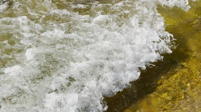 Bright white bubbles and frothy foam crash over a shallow riverbed. The fast movement of the water creates an exciting and powerful feeling of pure natural energy.