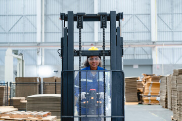African worker operates a forklift in a spacious warehouse filled with wooden pallets and cardboard boxes, wearing a blue uniform and hard hat, demonstrating focused operation and safety procedures. © AU USAnakul