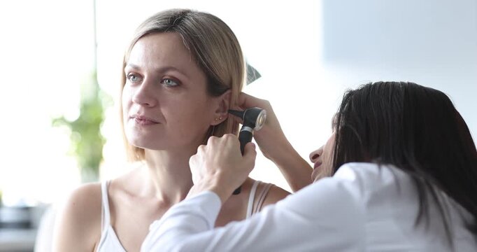 Woman otolaryngologist checks ear of lady patient with medical tool. Physician observes internal structures of ear during examination. Slow motion