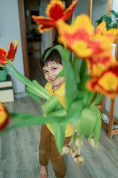 Smiling child in yellow shirt giving tulips for Women's Day indoors