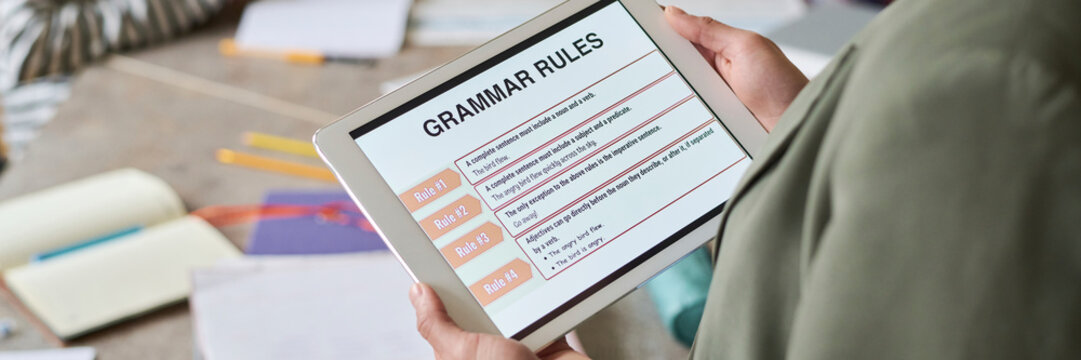 Student holding digital tablet with grammar rules on screen in classroom