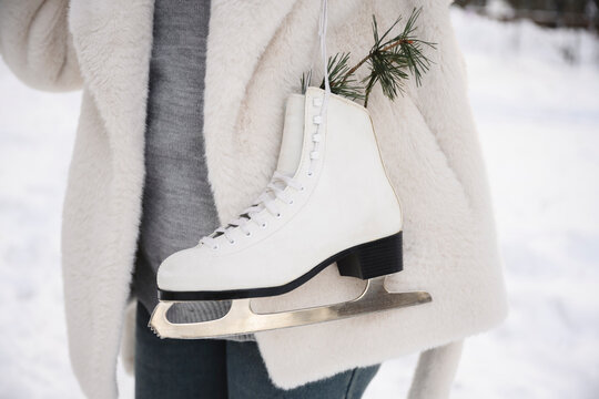 Ice skate and pine branch held outdoors in winter snow with warm clothing