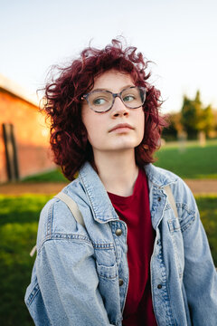 Confident teenage girl with curly hair in denim jacket at urban park