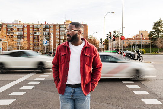 Man in red jacket walking at city crosswalk with blurred traffic
