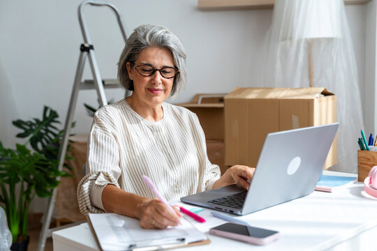 Smiling woman working on paperwork in a home office with a laptop
