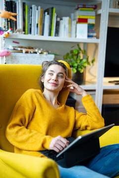 Woman relaxing in a yellow armchair at home with a tablet