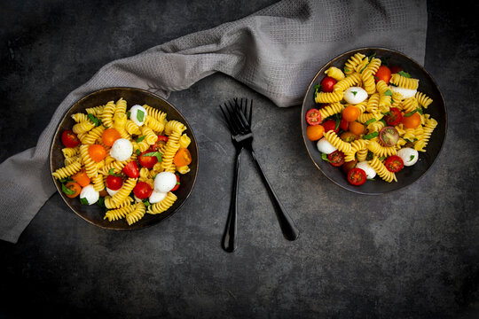 Pasta salad with mozzarella tomato and basil in bowls on dark background