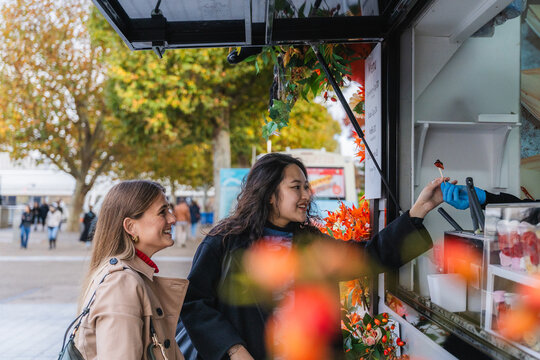 Friends smiling and buying street food at a truck in autumn city