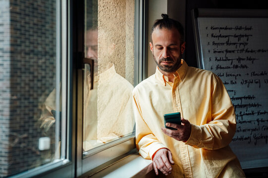 Business developer at window with smartphone in modern office
