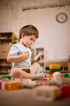 Little boy sitting on floor playing with colorful building blocks during focused playtime at home. Concept of fine motor skill development, early learning activities and toy product usage.