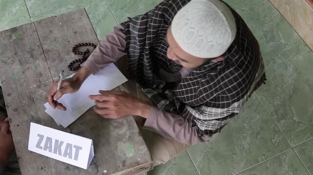 Zakat envelope exchange on wooden desk, hands passing cashfilled envelope while administrator counts notes and signs ledger next