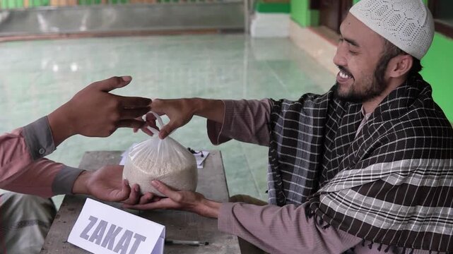 Asian man handing rice bag over zakat table, neighborhood donor meeting mosque volunteer, plastic sack of rice exchanged, friendly