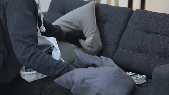 Criminal in Black Gloves Stealing Cash and Loot from a Sofa