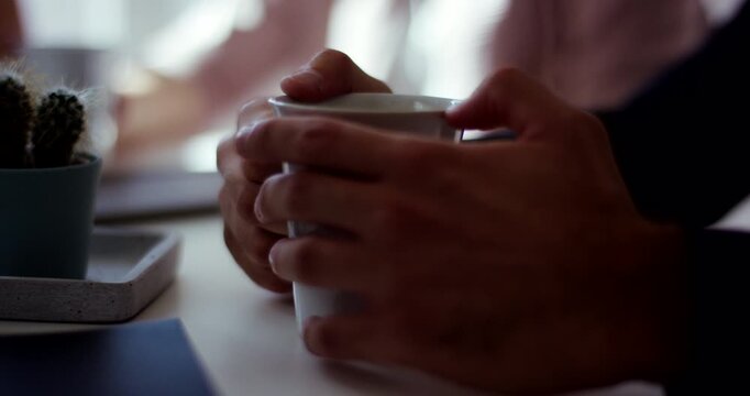 Extreme close up of human hands holding a white ceramic coffee cup during a meeting break indoors