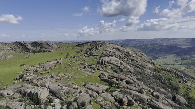 Drone flies over rocks and grass as clouds pass above on a sunny day at Sibebe Rock near Mbabane, Eswatini