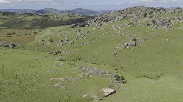 Drone flies high over green landscape dotted with gray rocks on a sunny day at Sibebe Rock near Mbabane, Eswatini