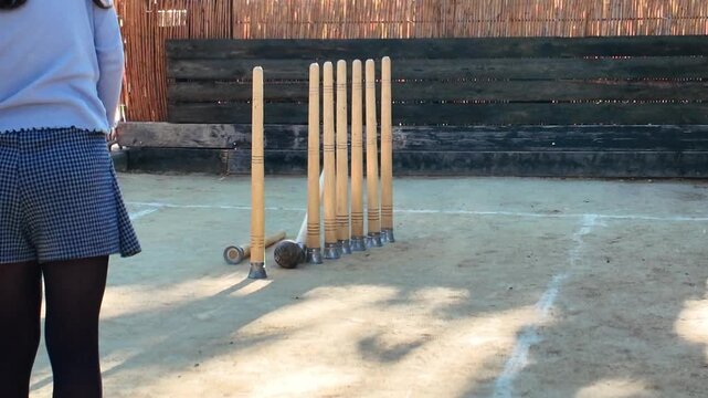 Player standing on a sandy court watching tall wooden pins and a ball during a traditional game of bolos huertanos outdoors highlighting cultural heritage and regional sports in Murcia