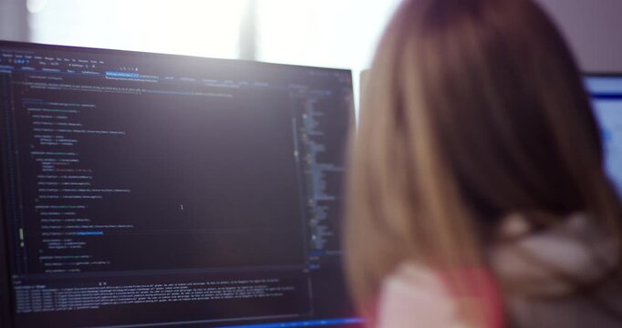 Software developer working on computer with source code on screen in office environment