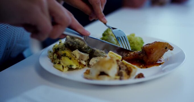 Close up of person cutting cooked meat with knife and fork on a white plate during lunch