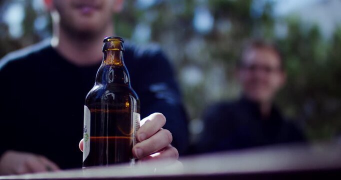 Close up of a person opening a brown glass bottle with a bunch of keys outdoors in nature