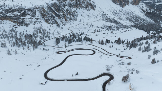 Aerial view of the Cappella di San Maurizio and a winding mountain road through the snow-covered Dolomites in Selva di Val Gardena, Trentino-Alto Adige, Italy.