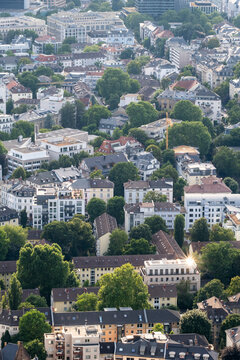 Frankfurt city skyline seen in summer from an aerial viewpoint over neighborhood rooftops and urban buildings with trees shaping the landscape