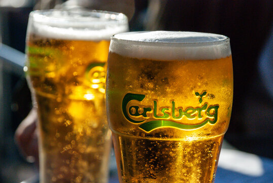 Two pints of Carlsberg lager on a table outside in the summer with sun shining through the glasses 