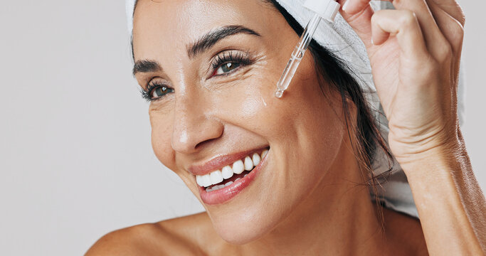Skincare, thinking and woman with dropper in studio, hyaluronic acid treatment and anti aging serum. Smile, dermatology or mature person apply product for glowing skin, reflection or white background