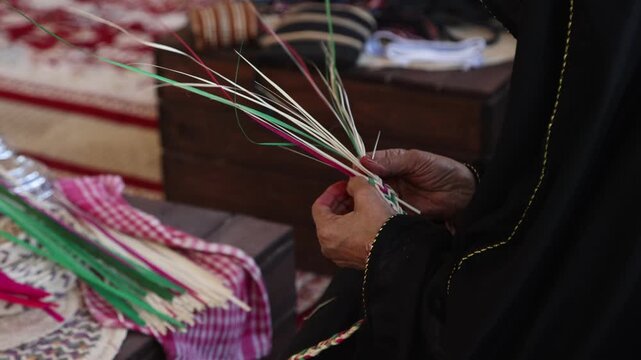 Emirati woman artisan weaving traditional Al Khous from dried palm leaves, closeup on hands. UAE heritage and sustainable craft concept.