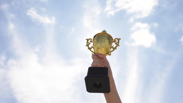 Raised hand holding trophy against sky in outdoor setting. Concept of achievement, success, victory, motivation, and recognition. Symbol of excellence and winning spirit.