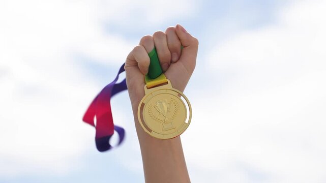 Close-up of hand holding medal outdoors with sky background. Represents achievement, victory, success, and recognition. Ideal for award, competition, and motivation themes.