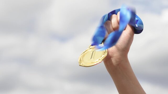 Hand holding gold medal with sky background in outdoor scene. Concept of success, achievement, reward, and victory. Motivation and recognition for effort and excellence.
