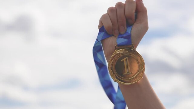 Close-up of a raised hand holding a medal against the sky. Represents achievement, success, victory, and recognition. Ideal for motivation, competition, and award concepts.
