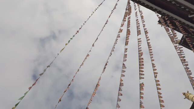 Low angle shot of colorful Tibetan prayer flags waving in the wind against a cloudy sky at the historic Ganden Sumtseling Monastery in Yunnan.
