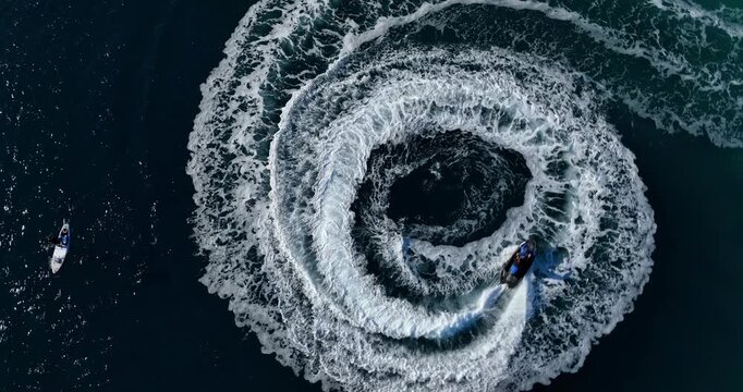 A high-speed motorboat maneuvers in tight circles, creating a white foam spiral on blue water.