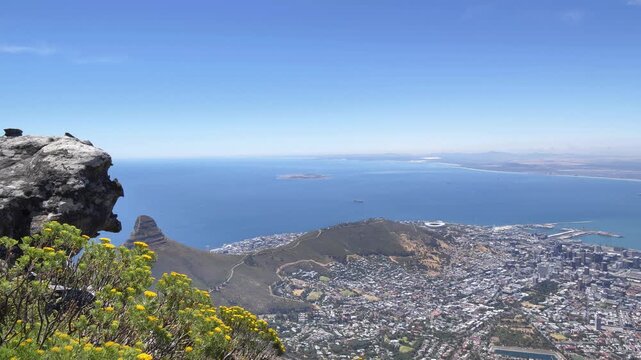 A spectacular aerial perspective showcases the vibrant cityscape of Cape Town, Robben Island, and the Atlantic seaboard nestled beside the vast blue ocean, with Lion's Head prominent in the distance.