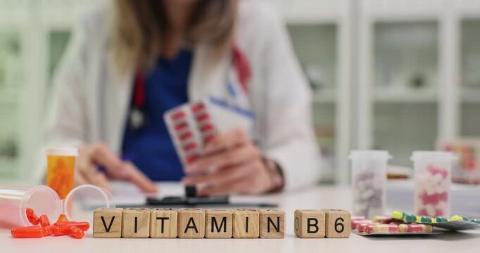 Woman dietitian writes vitamins prescription for patient holding tablets in hand. Wooden cubes on desk clearly form phrase Vitamin B6 as treatment
