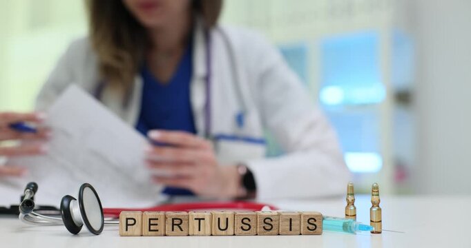 Wooden blocks spell word Pertussis on desk near ampoules and stethoscope. Lady doctor writes record scheduling vaccine dose for cough prevention
