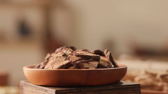 Reddish-brown root slices arranged in wooden bowl. Rotating close-up highlights grain patterns and earthy tones of traditional herbal medicine ingredient.