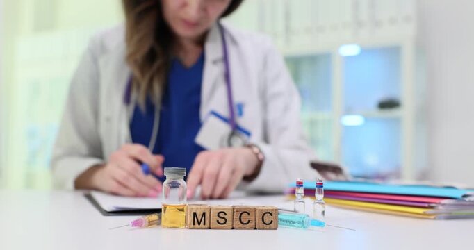 Wooden blocks spell abbreviation MSCC near ampoules and papers on desk. Doctor fills chart reviewing oncology notes while marking next diagnostic step
