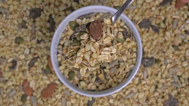 Top view of hand scooping granola from bowl with spoon on a textured cereal background