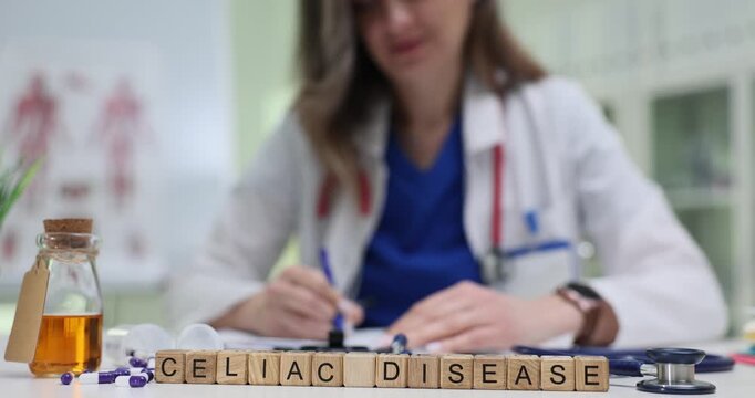 Wooden blocks spell phrase Celiac Disease near bottles and stethoscope. Doctor writes record listing symptoms while ordering gluten test for diagnosis