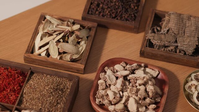 Assorted dried herbal ingredients arranged in wooden trays and bowls. Variety of roots, slices and cubes highlights traditional Chinese medicine materials and natural apothecary display.